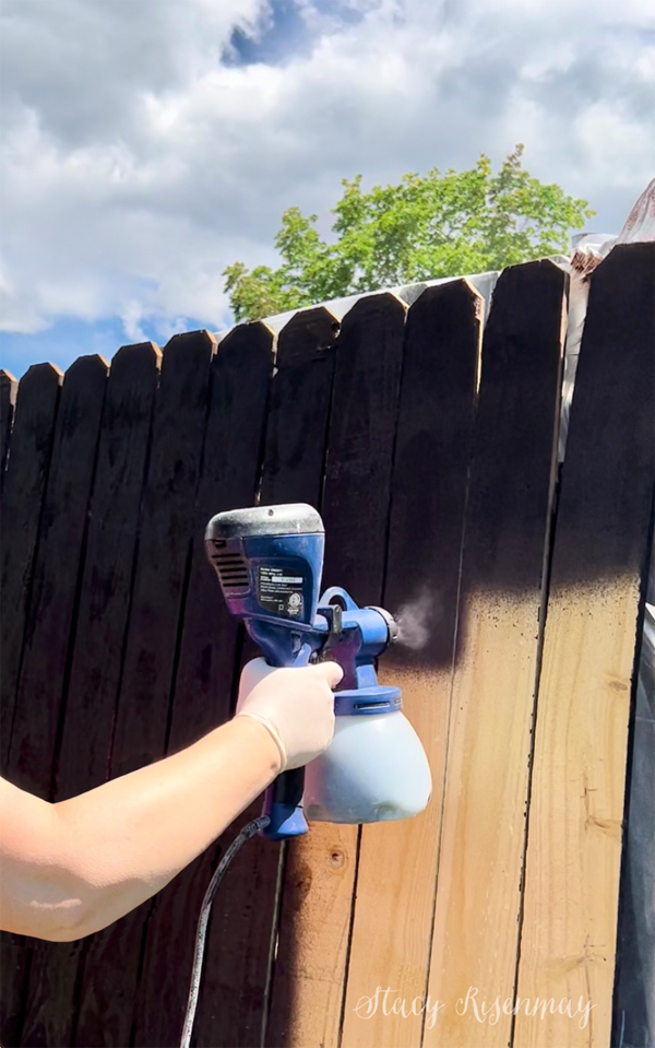 spraying stain on a fence